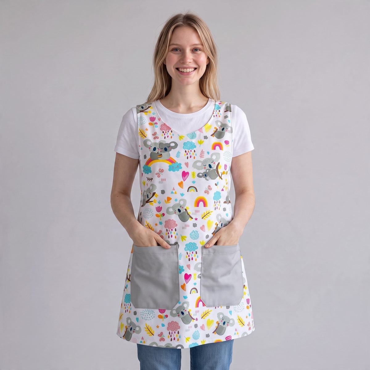 Bata de maestra SuYa Shop blanca con estampado de koalas, arcoíris y corazones, con dos bolsillos frontales grises.