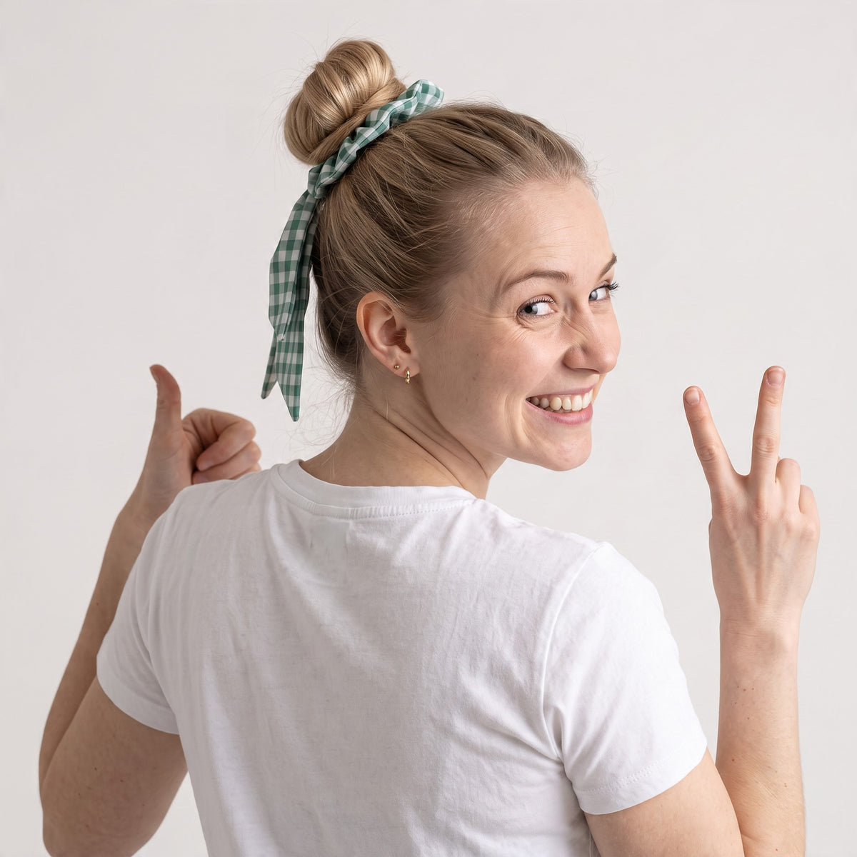 Coletero BEE de SuYa Shop, scrunchie de algodón verde con cintas largas extraíbles en el pelo de una modelo sonriente.
