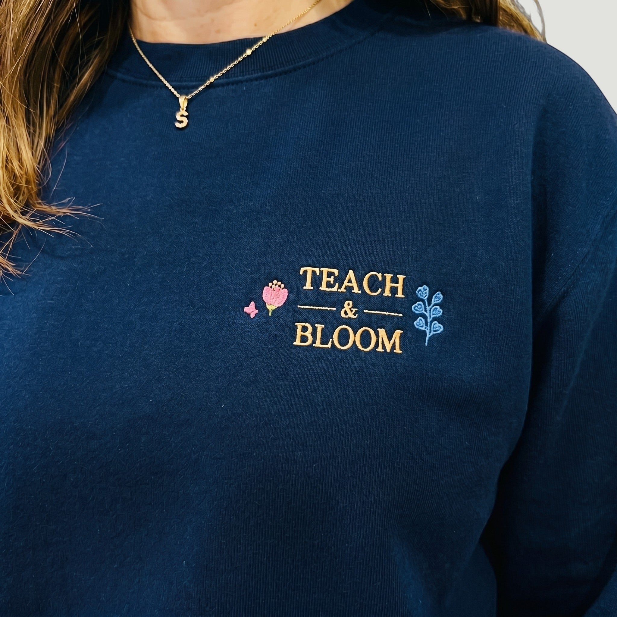 SuYa Shop navy blue sweatshirt featuring Teach and Bloom floral embroidery on the chest for teachers.