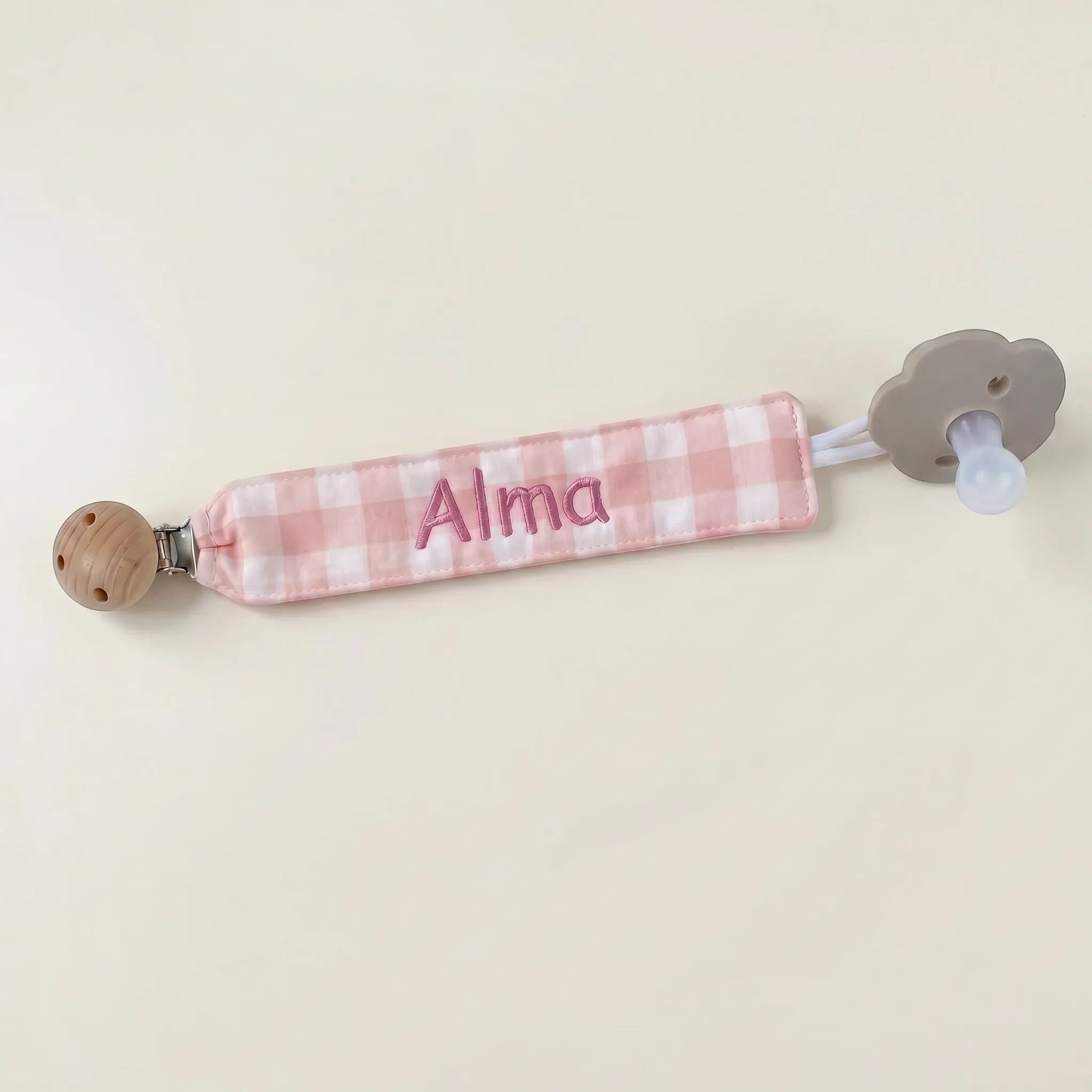 SuYa Shop personalized pink gingham fabric pacifier clip with Alma embroidered and a grey flower-shaped pacifier