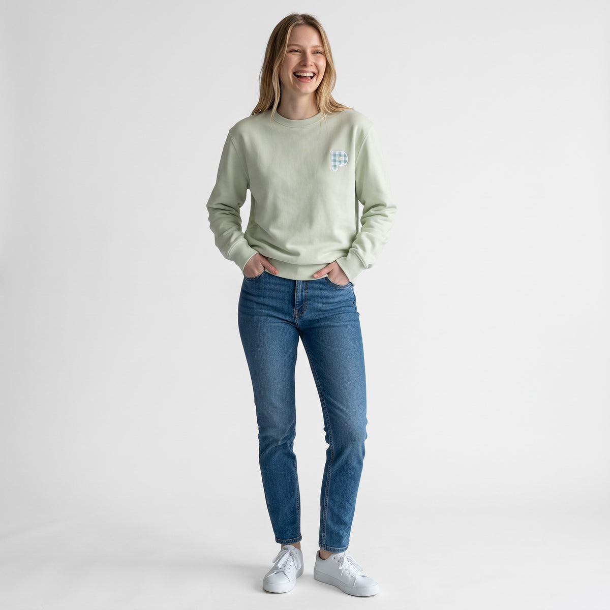 Modelo sorridente com sweatshirt SuYa Shop cor de menta, inicial em estampado vichy e calças de ganga azuis