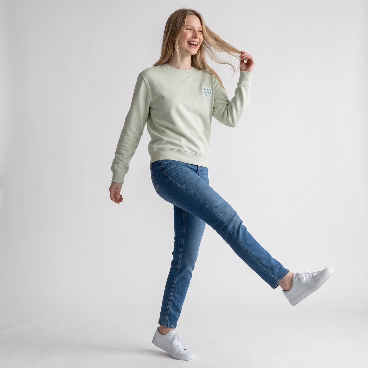 Modelo sorridente a usar uma sweatshirt SuYa Shop cor de menta com inicial em estampado vichy e calças de ganga azuis