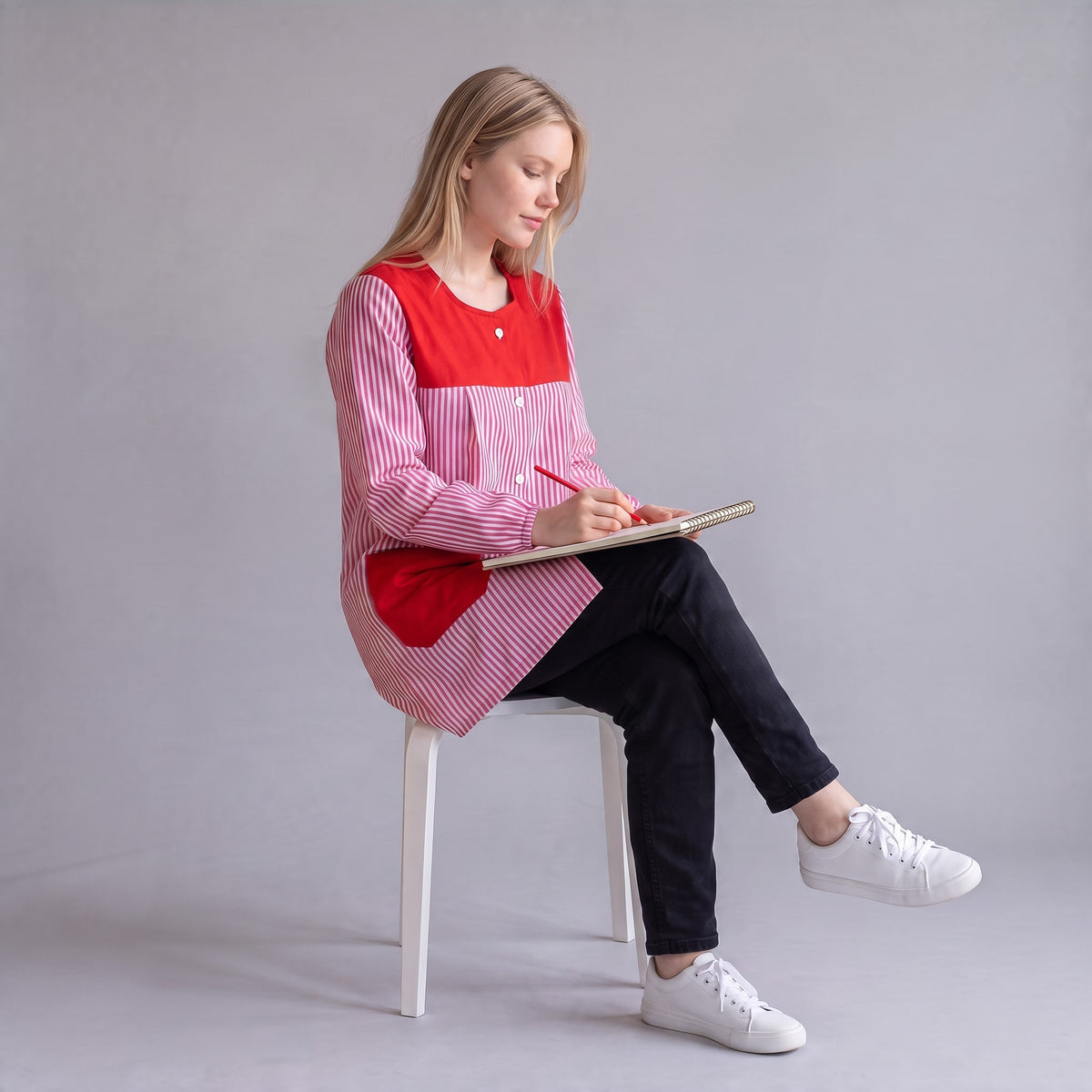Profesora con bata SuYa Shop de rayas rojas y blancas escribiendo en un cuaderno sobre fondo gris