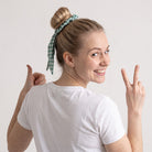 Coletero BEE de SuYa Shop, scrunchie de algodón verde con cintas largas extraíbles en el pelo de una modelo sonriente.