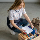 SuYa Shop sleeveless teacher apron with floral pattern and navy blue details, worn by a woman organizing school supplies