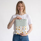 Mujer sonriente sosteniendo una funda acolchada SuYa Shop con estampado de abejas y flores y parte superior de cuadros
