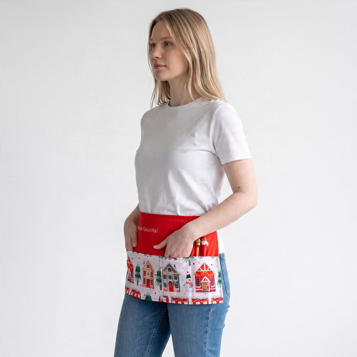 Mulher a usar um avental de Natal vermelho da SuYa Shop com estampado de casas com neve e bolsos frontais