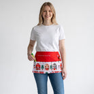 Mulher a usar um avental de Natal vermelho da SuYa Shop com estampado de casas e o texto "Mi estación favorita"