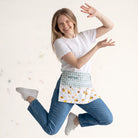 Mujer saltando feliz usando un mandil personalizado SuYa Shop con estampado de abejas, flores y bolsillo con cremallera