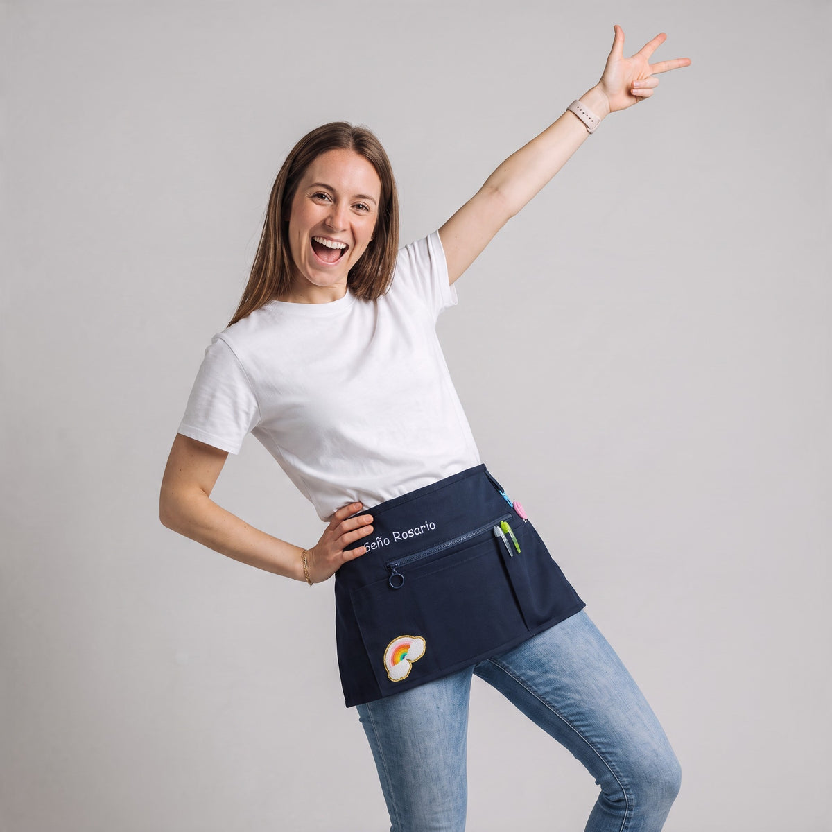 Profesora sonriente usando un mandil vaquero azul marino personalizado de SuYa Shop con parche de arcoíris y bordado.