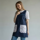 SuYa Shop navy blue teacher smock with floral pockets and personalized embroidery worn by a smiling woman