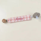 SuYa Shop personalized pink gingham fabric pacifier clip with Alma embroidered and a grey flower-shaped pacifier