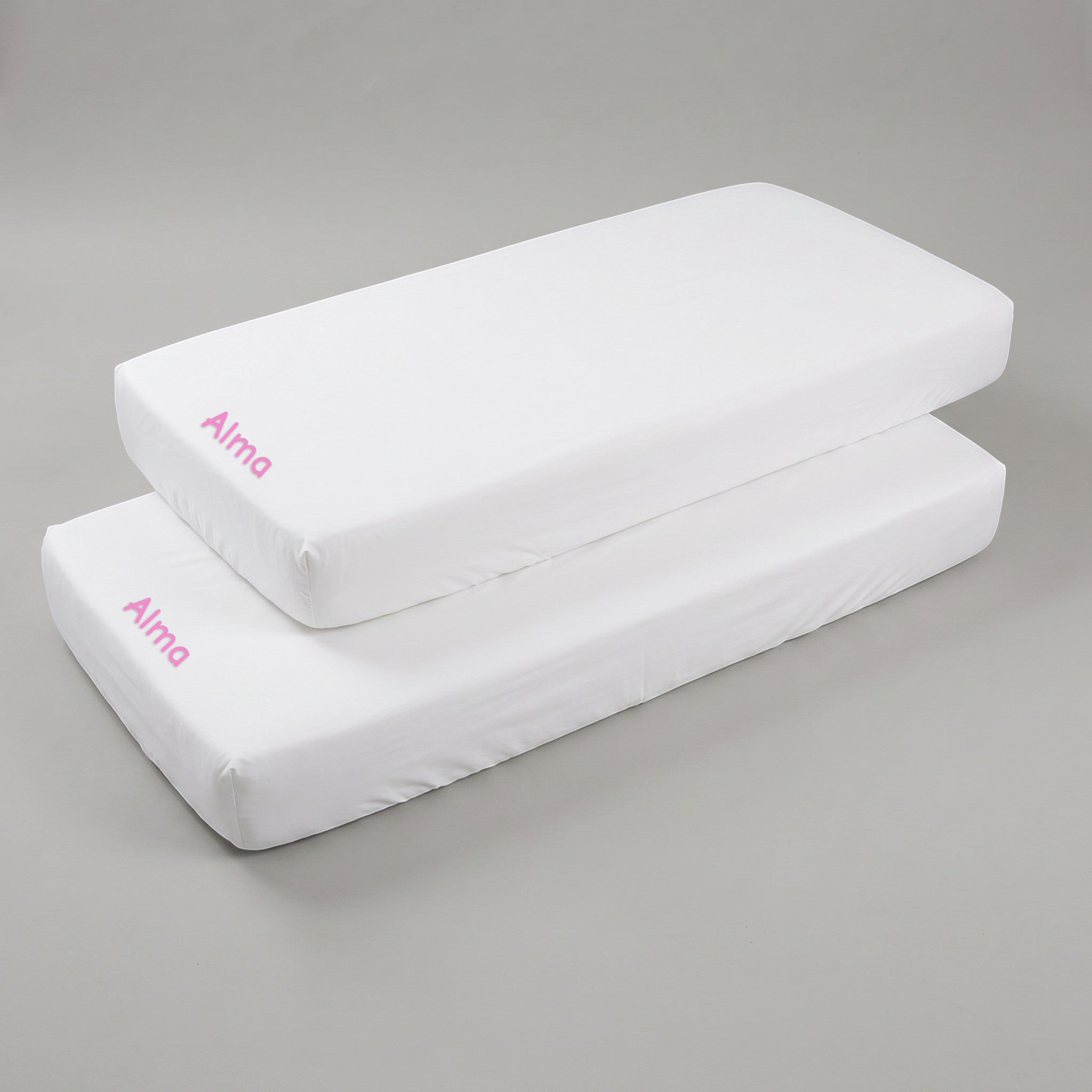 Two white SuYa Shop cotton crib sheets for 120x60cm mattresses, each personalized with the name Alma in pink text.