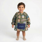 SuYa Shop toddler school smock in olive green with sports print, elastic cuffs, and a personalized navy blue pocket.